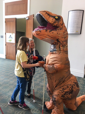 Girls shaking hands with inflatable T-Rex.